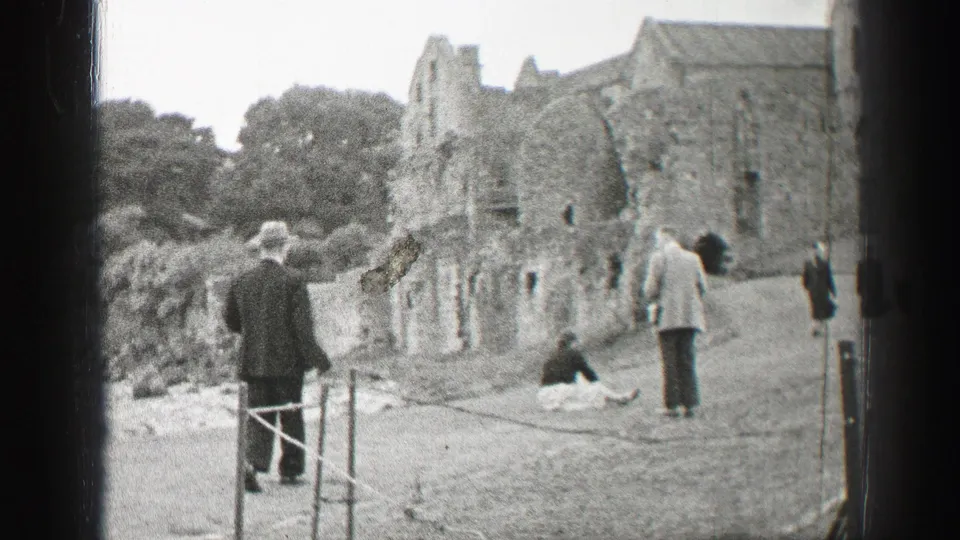 Tourists at a United Kingdom historic ruin in 1952, with rope posts, grassy ground, and weathered masonry visible.