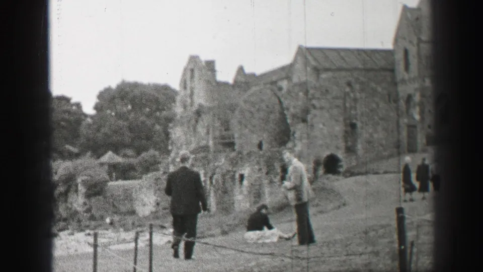 Final frame of tourists at a 1952 United Kingdom stone ruin, with standing figures, trees, and roped pathways visible.