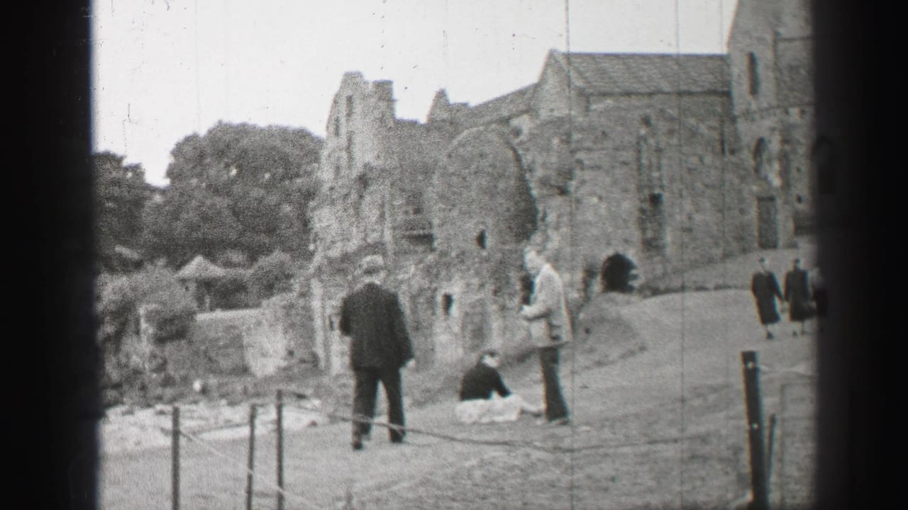 Visitors stand and walk near stone church ruins beside a roped path.