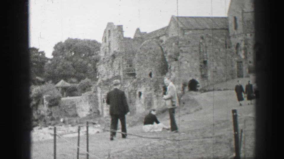 1952 United Kingdom 8mm frame showing well-dressed visitors near stone church ruins and a roped walkway.