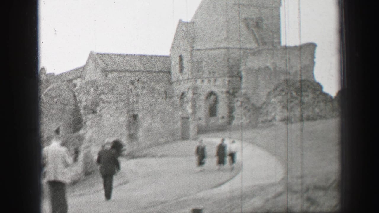 Visitors in formal coats walk uphill toward historic stone church ruins in the United Kingdom, filmed on 8mm in 1952.