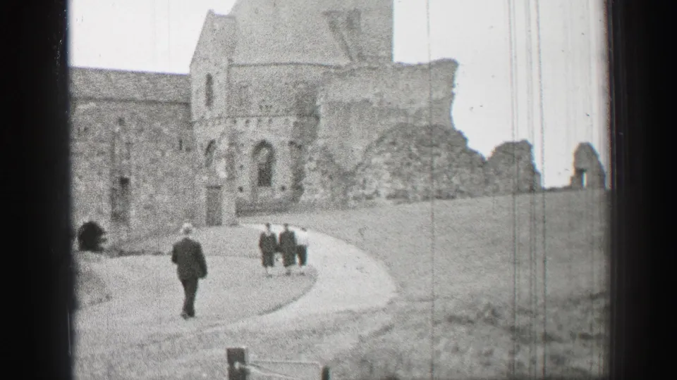 Well-dressed visitors move along the curved path beside stone church ruins in United Kingdom 8mm footage from 1952.