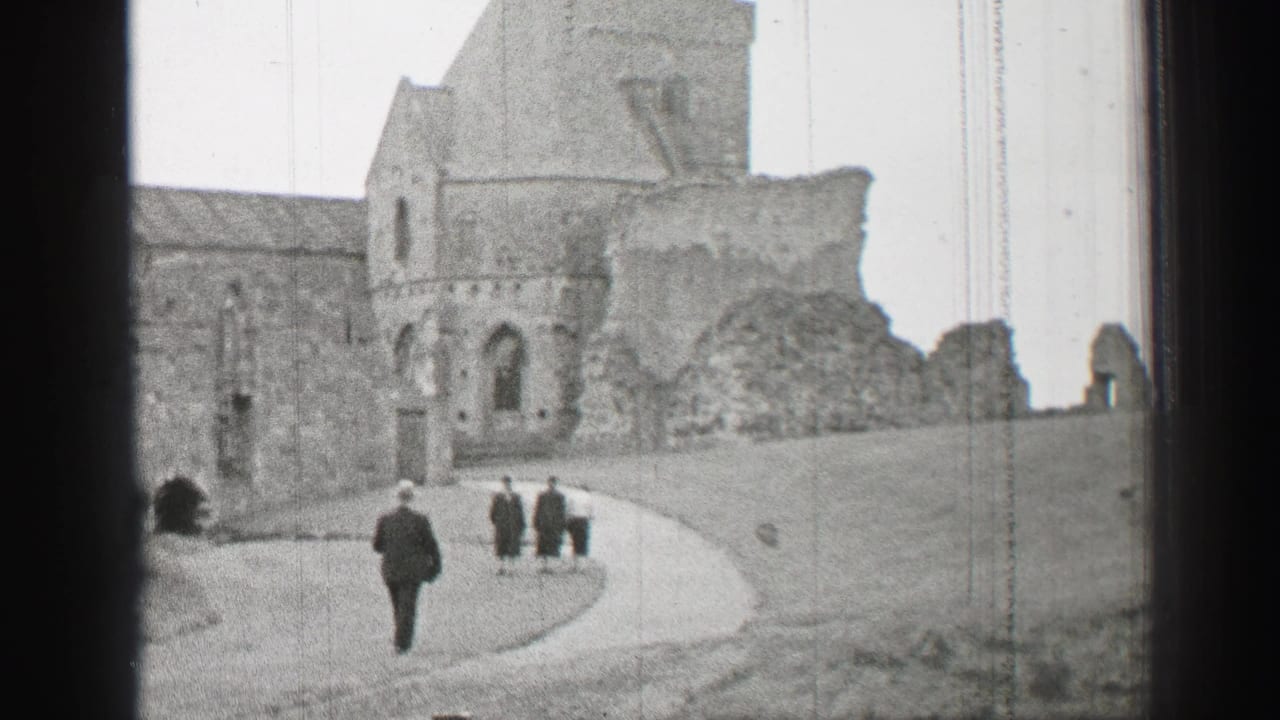 Visitors walk along a curved path toward stone castle ruins.