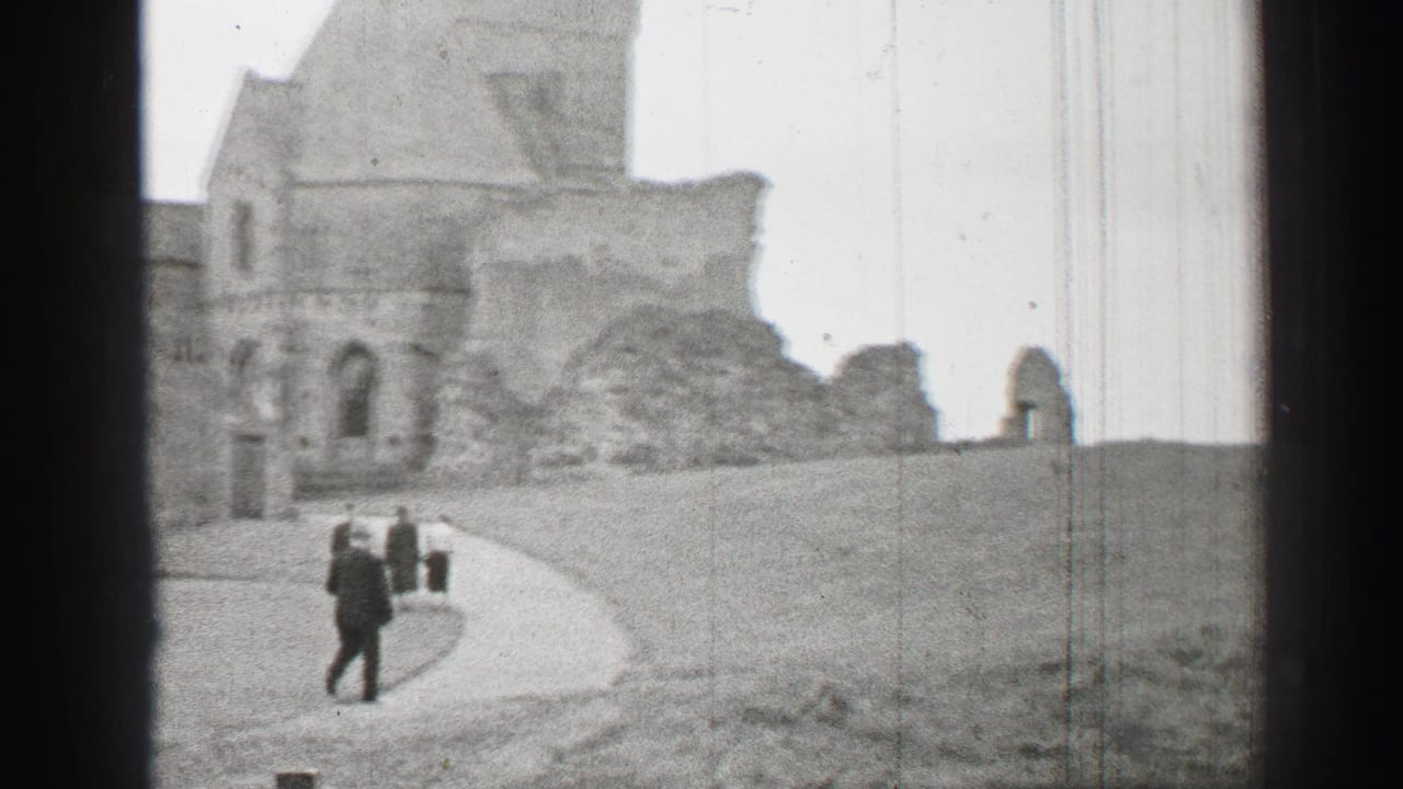 1952 United Kingdom 8mm frame with a formally dressed visitor walking near castle ruins and a curved path.