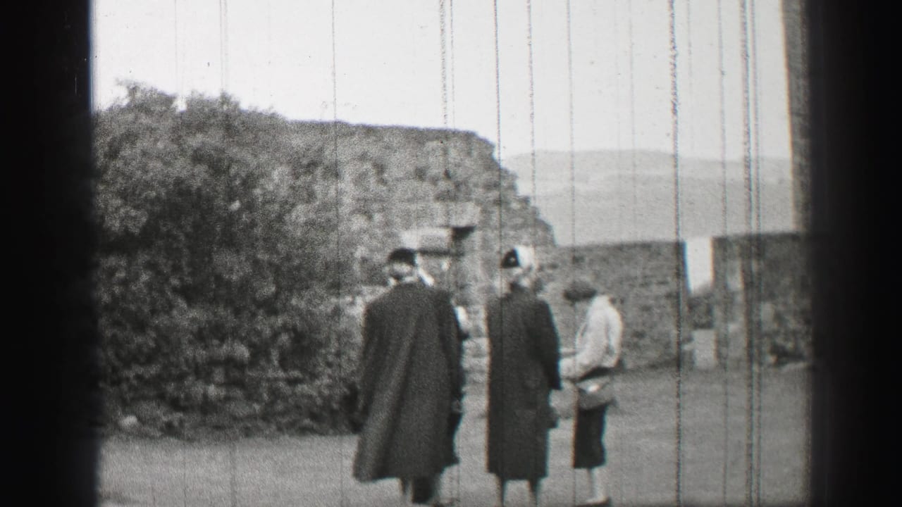Three women stand in a stone courtyard beside shrubs and old walls.