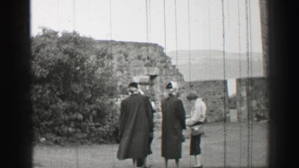 Three women in coats and hats stand in a United Kingdom stone courtyard in 1952 home-movie footage.