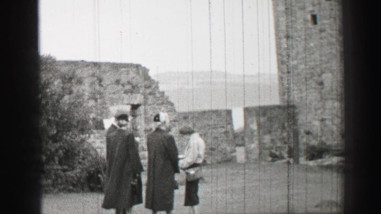 Women in mid-century coats and hats gather near stone walls during a United Kingdom castle courtyard visit.