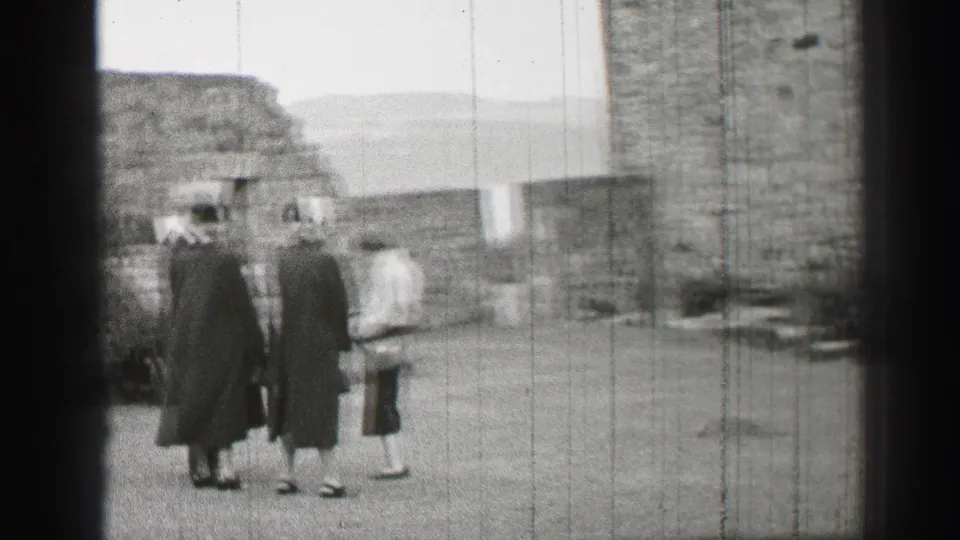 Three women walk away through a stone courtyard in black-and-white 1952 United Kingdom home-movie footage.