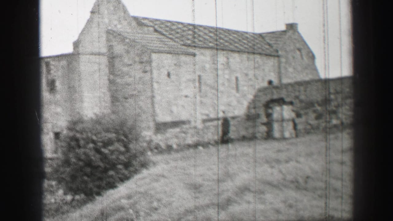 1952 United Kingdom 8mm frame showing an older stone building, grass yard, bushes, and arched wall openings.