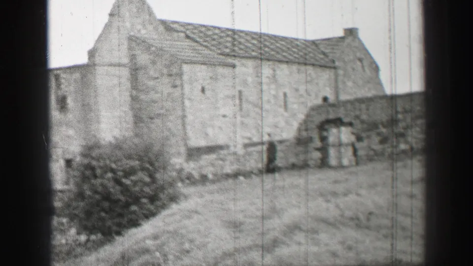 1952 United Kingdom 8mm frame showing an older stone building, grass yard, bushes, and arched wall openings.
