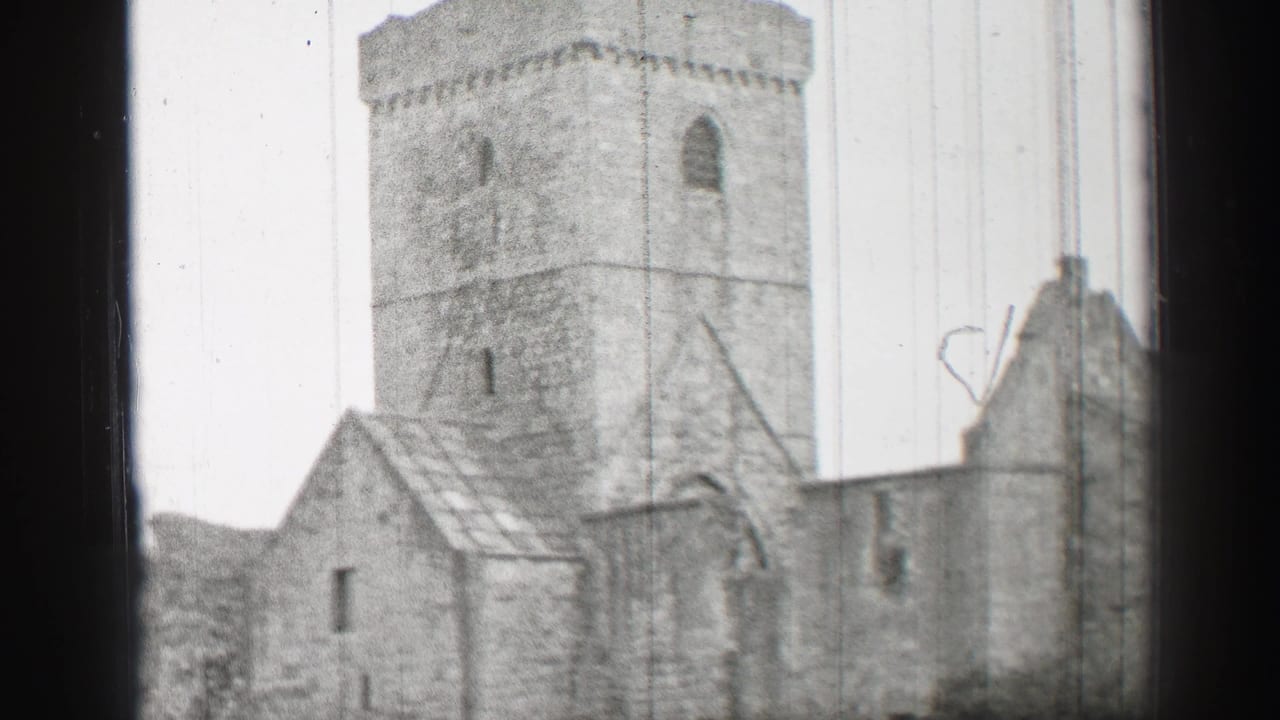 1952 United Kingdom 8mm frame showing a weathered stone ruin with a square tower, rooflines, arched opening, and perimeter wall.