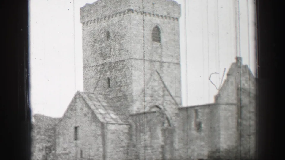 1952 United Kingdom 8mm frame showing a weathered stone ruin with a square tower, rooflines, arched opening, and perimeter wall.