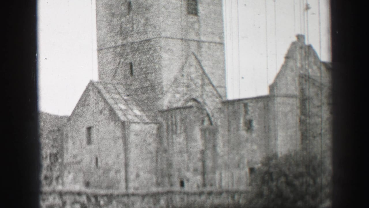 1952 United Kingdom home-movie frame of a stone ruin with a tower, gabled sections, narrow windows, and a high wall.