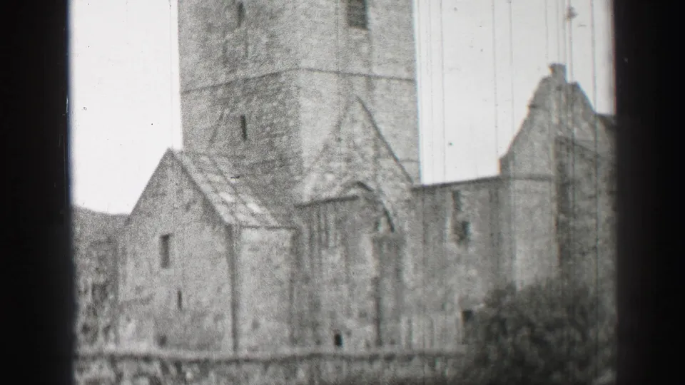 1952 United Kingdom home-movie frame of a stone ruin with a tower, gabled sections, narrow windows, and a high wall.