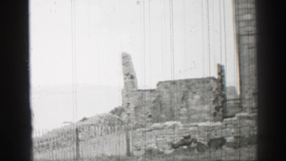 1952 United Kingdom home-movie frame showing lower ruined walls, a broken upright masonry section, and a tall stone edge at right.