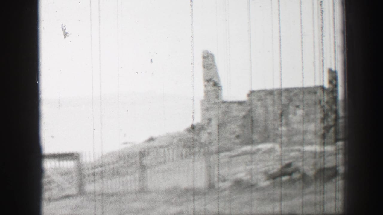 1952 United Kingdom 8mm frame showing a weathered stone ruin, fencing, and a grassy slope in soft black-and-white focus.
