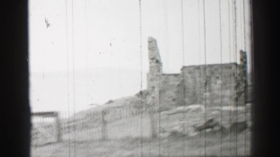 1952 United Kingdom 8mm frame showing a weathered stone ruin, fencing, and a grassy slope in soft black-and-white focus.