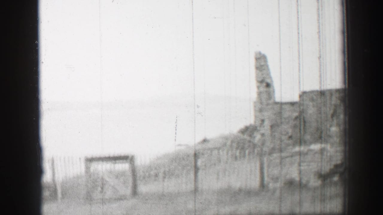 1952 United Kingdom 8mm frame with a closed wooden gate, fence posts, grassy ground, and partial stone ruin in the distance.