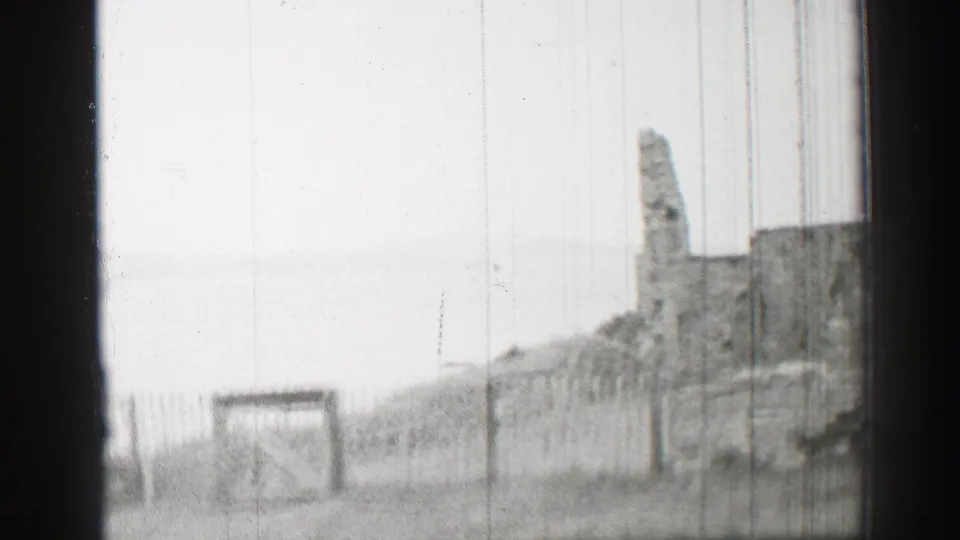 1952 United Kingdom 8mm frame with a closed wooden gate, fence posts, grassy ground, and partial stone ruin in the distance.