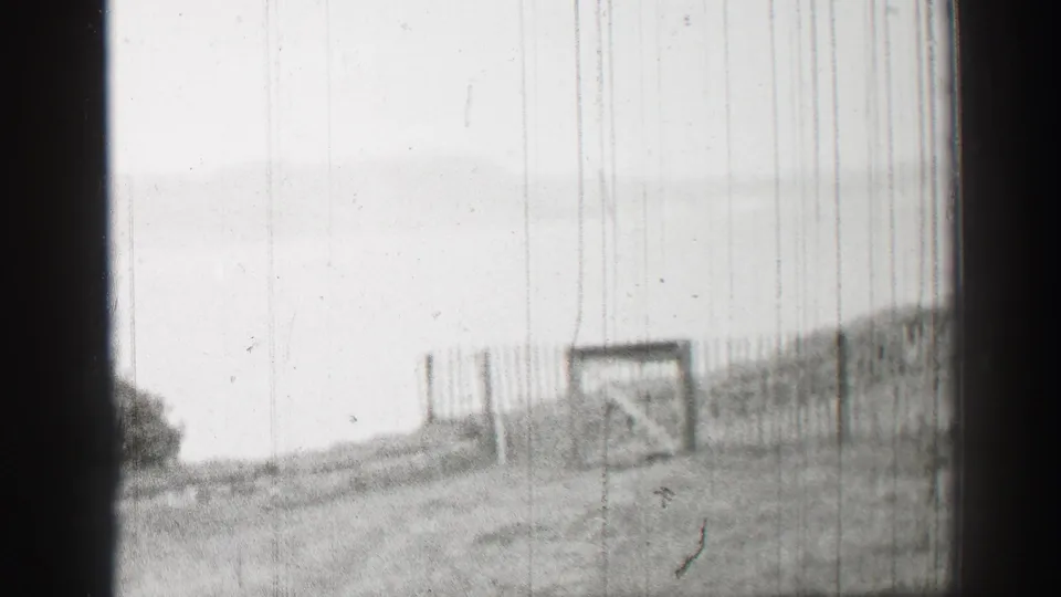 1952 United Kingdom 8mm frame showing a closed gate, sloped fencing, and pale sky as the pan moves away from the ruin.