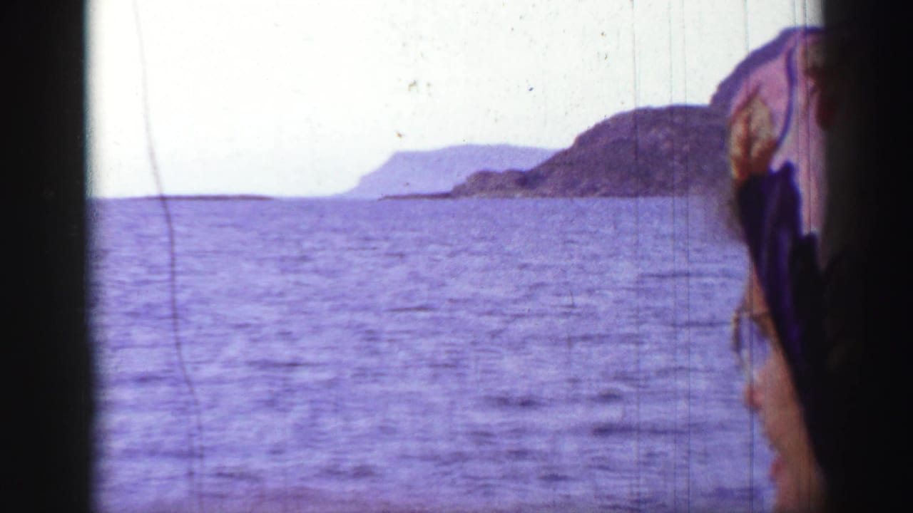Sea and distant rocky island seen through a window beside part of a woman's headscarf.