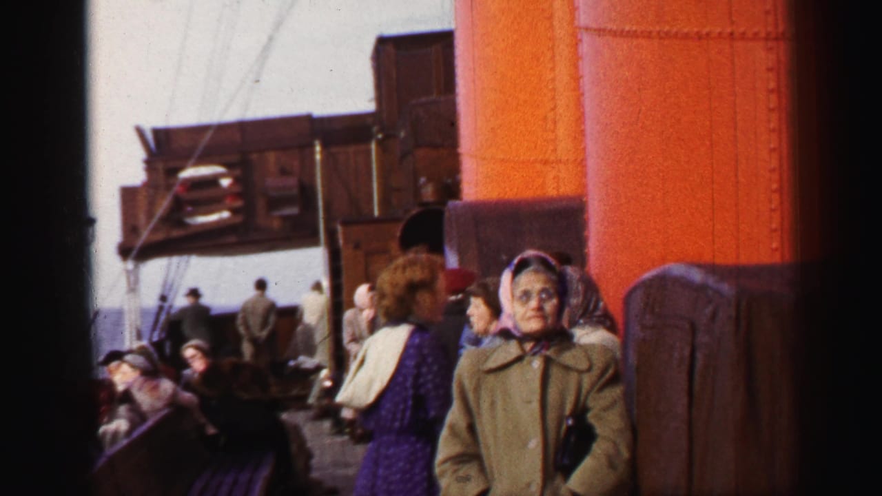 1952 8mm frame showing passengers in coats and headscarves gathered on a ship deck near a large orange smokestack.