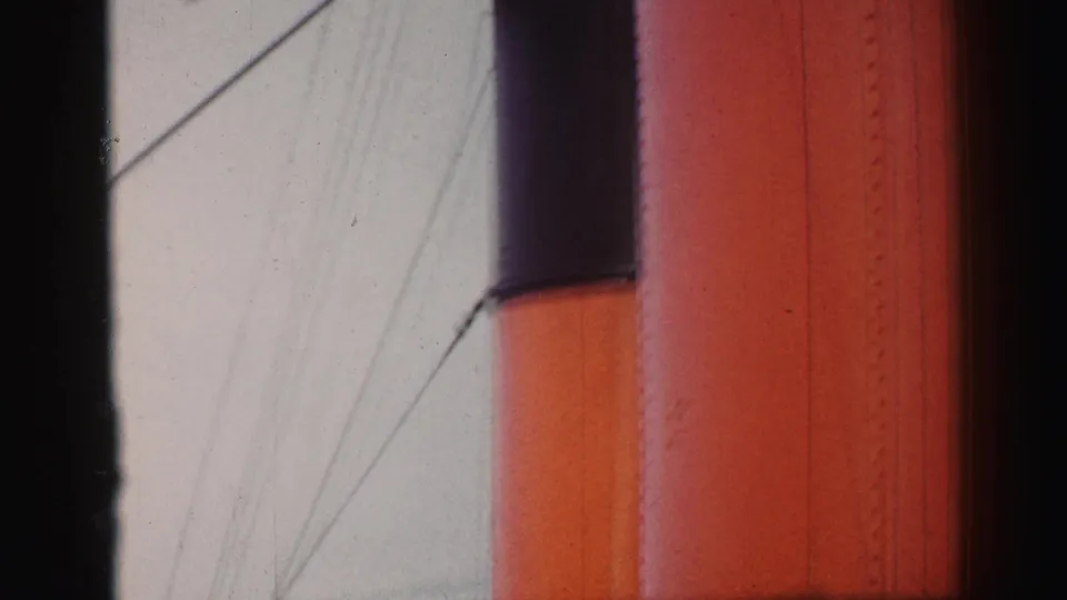 1952 8mm frame focused on the ship's orange and dark smokestack with rigging lines crossing a pale sky.