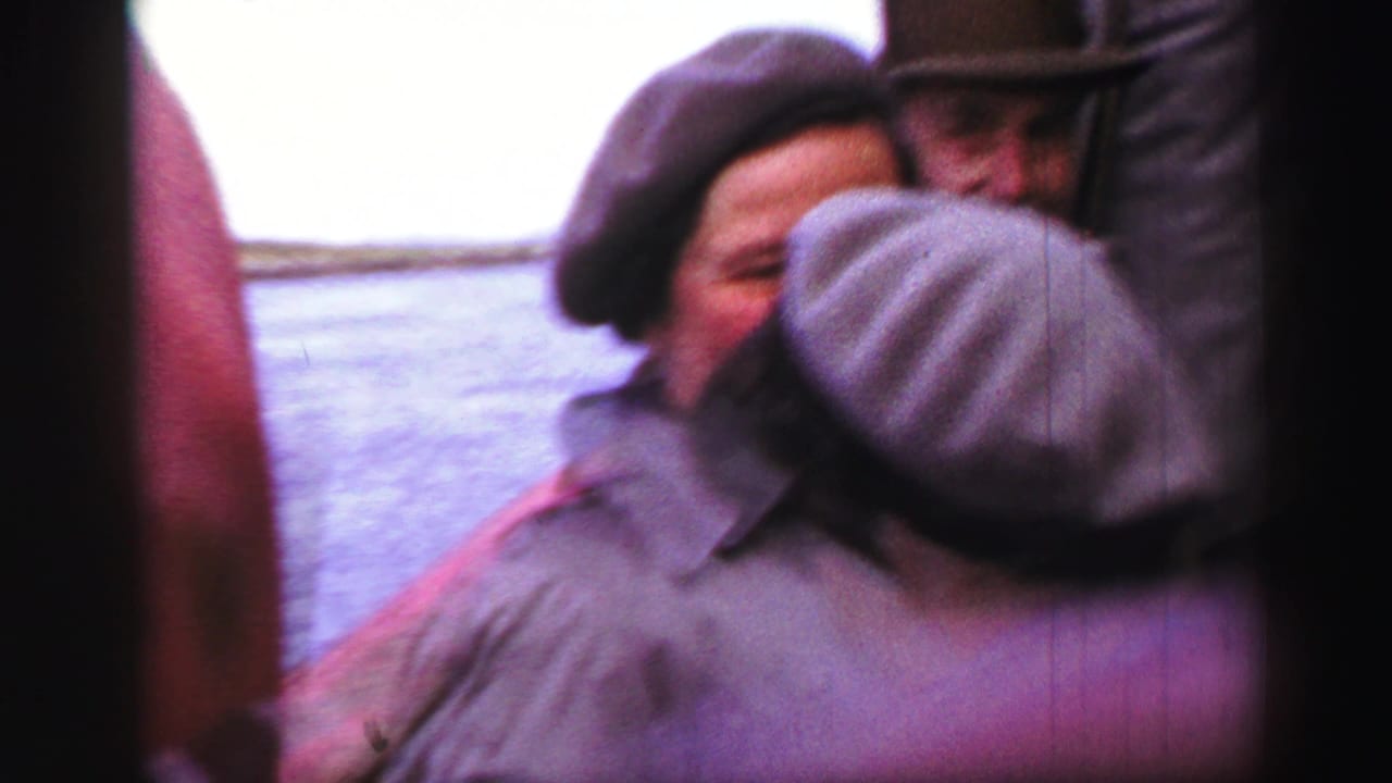 Two well-dressed adults in mid-century hats and coats pass close to the camera during a United Kingdom sightseeing moment.
