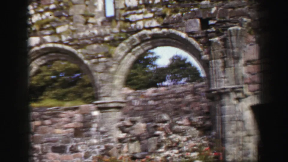 Large arched stone openings and broken masonry frame the historic ruin, with trees visible through the arches.