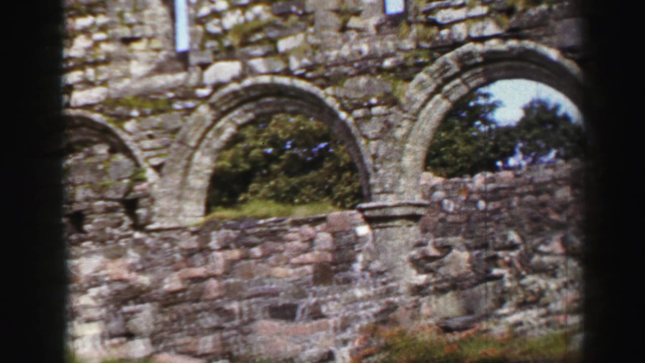 1952 United Kingdom home-movie frame showing arched stone ruins, rough masonry, greenery, and dark film gate edges.