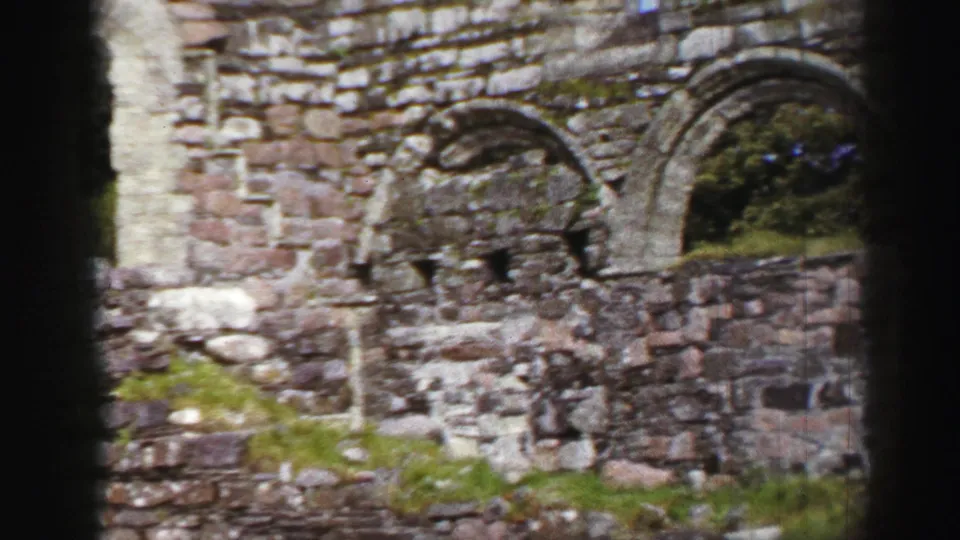 1952 United Kingdom view across rough stone walls and an arched opening, with mossy surfaces and trees beyond.