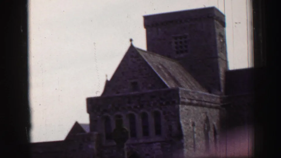 A historic stone church exterior appears with a square tower, arched windows, and a dark figure or shadow near the foreground.