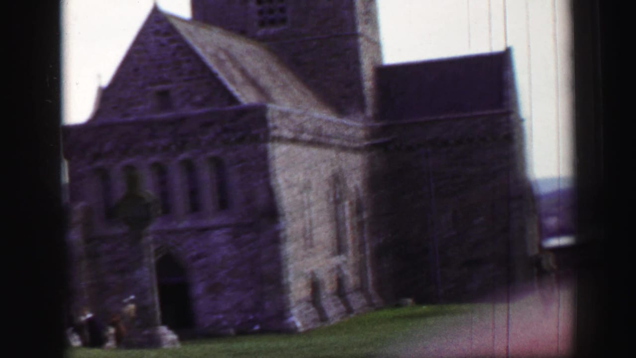 Stone church or abbey tower and arched entrance with grass in the foreground.