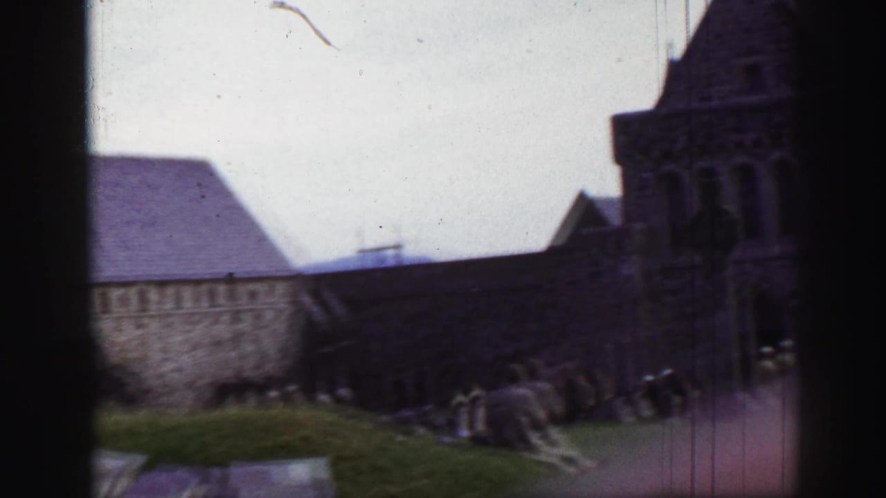 Long stone church or abbey building with tower, grass, and grave markers.