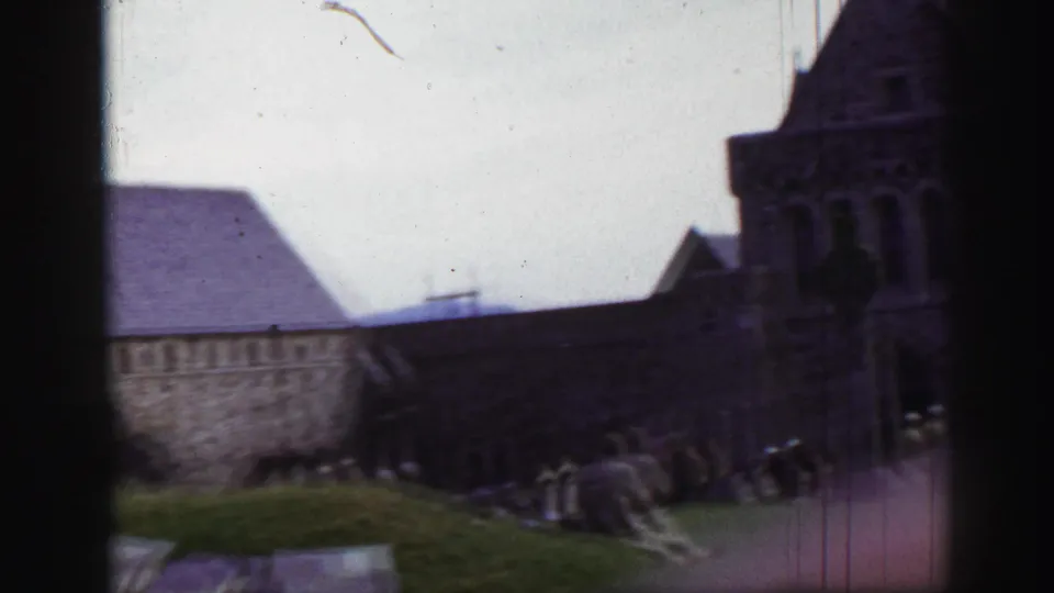 1952 United Kingdom 8mm frame showing a stone church or abbey range, tower, grassy yard, and scattered grave markers.