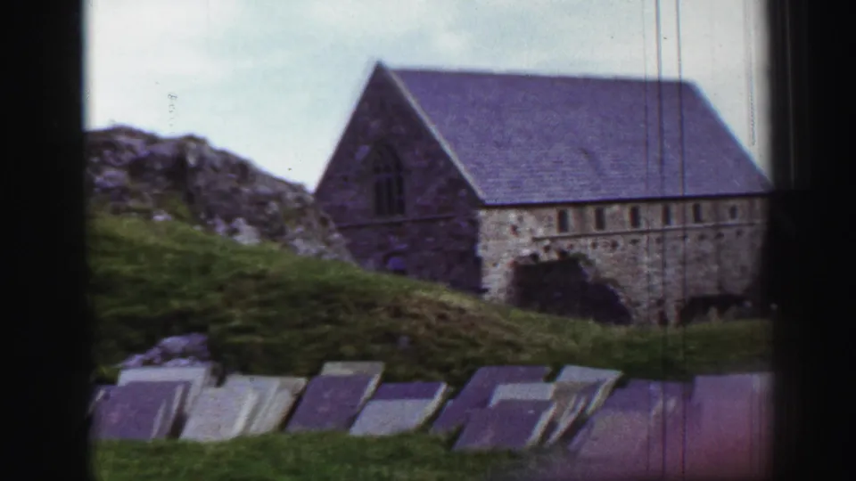 1952 United Kingdom 8mm view of a low stone church or abbey building behind a grassy slope and foreground grave slabs.