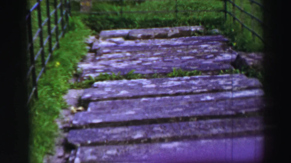 1952 United Kingdom 8mm frame showing a worn wooden walkway through grass with dark railings along the sides.