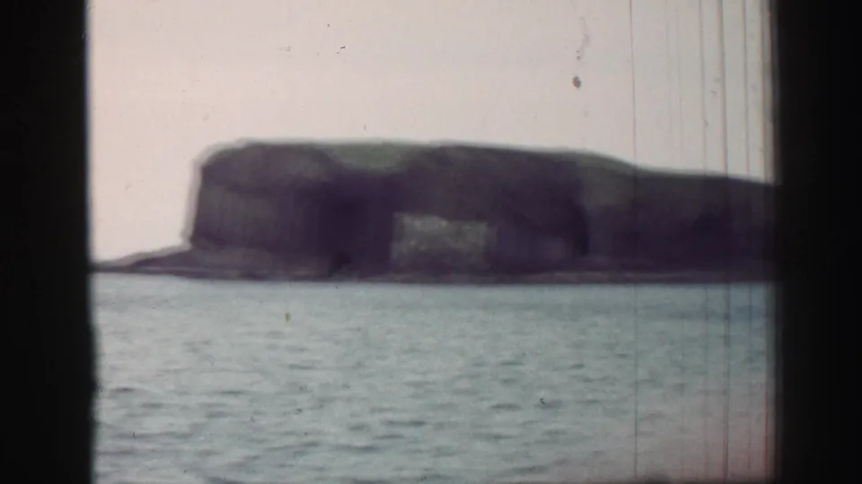 The view opens to calm coastal water and a dark rocky cliff or sea stack, consistent with the United Kingdom seaside metadata.