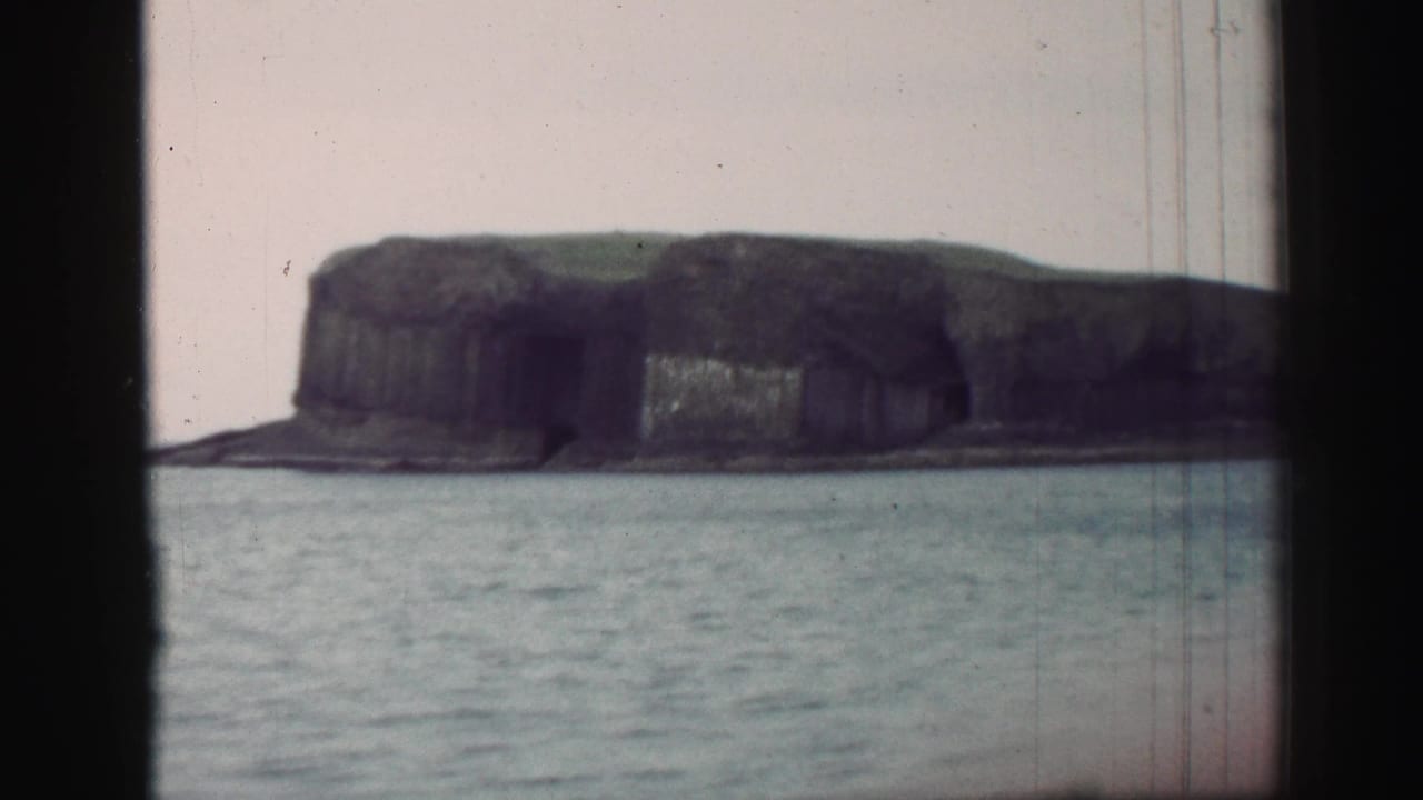 Coastal cliff across open water framed by dark vertical window edges.