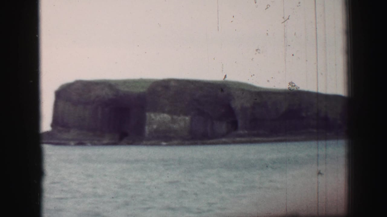 Rugged coastal cliff and grassy top seen across a body of water.