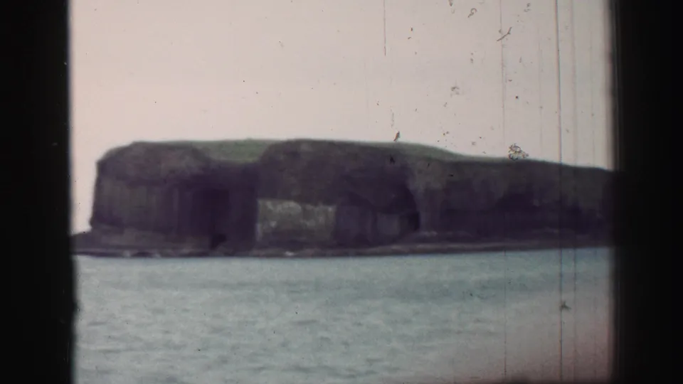 1952 United Kingdom coastal view showing a dark cliff face and grassy high ground across open water.