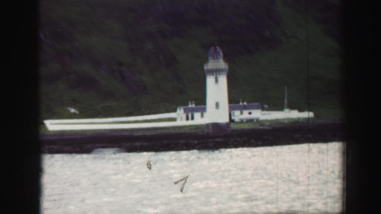 White lighthouse and keeper buildings on a rocky shoreline.