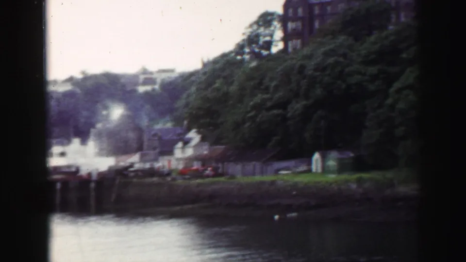 1952 United Kingdom harbor view with waterfront houses, docks or boats, trees, smoke, and buildings rising on the hillside.