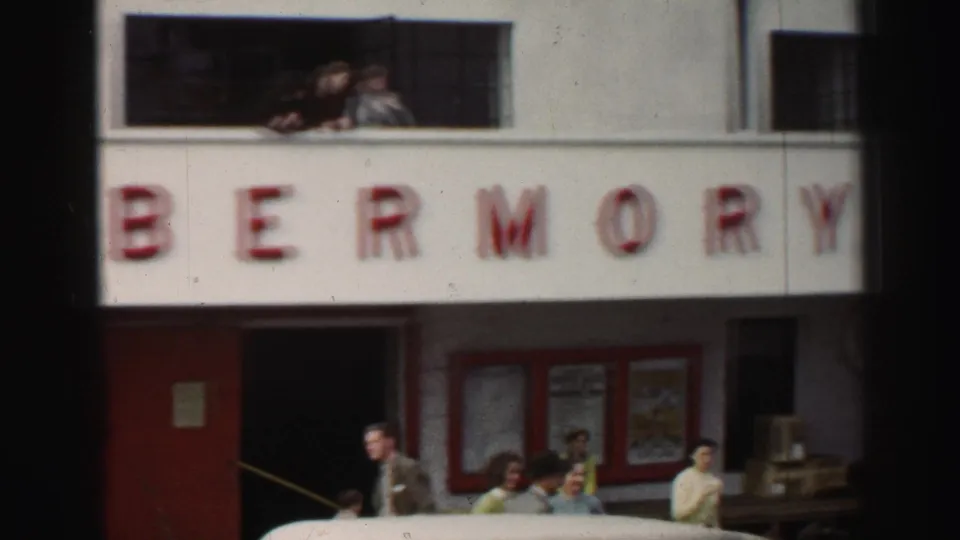 The red TOBERM sign fills much of the frame while people lean from a window and bystanders gather near the lower doorway and noticeboards.