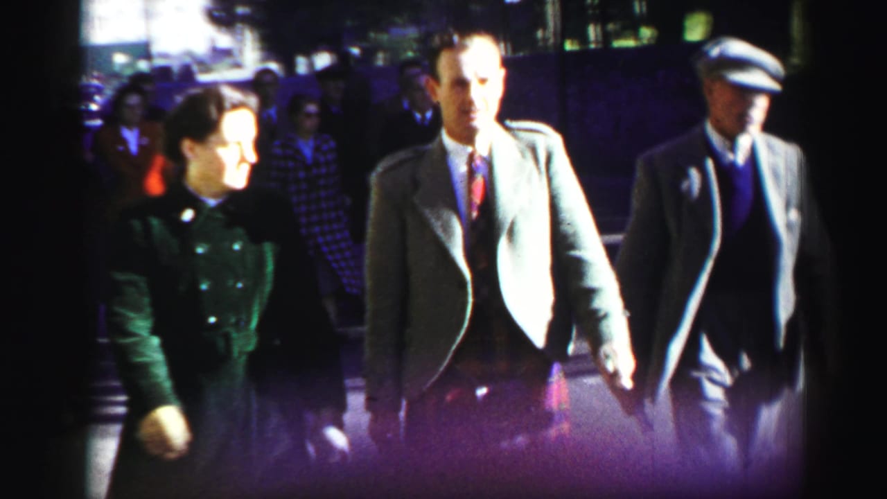 A woman and several men, including one in a kilt and one in a flat cap, walk along a crowded street.