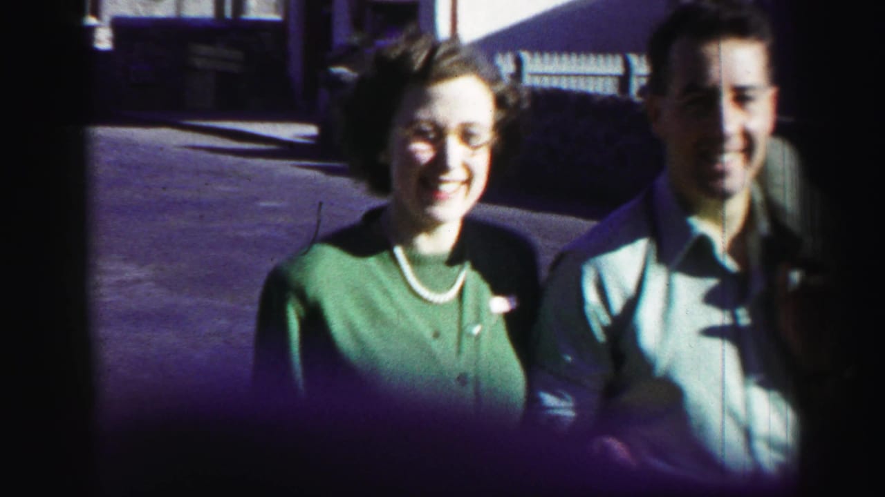 Older woman in a green cardigan stands beside a smiling man outdoors.