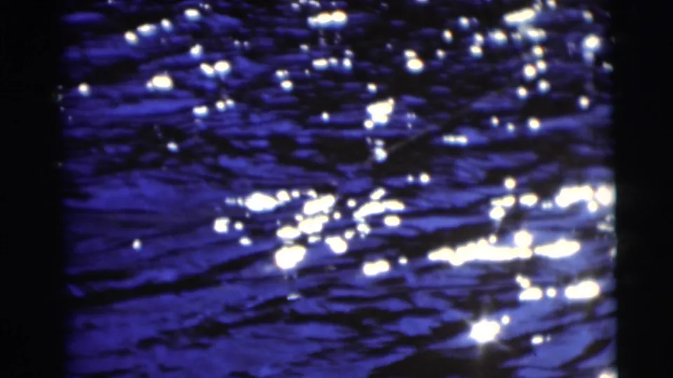 1953 8mm frame of dark blue water with scattered white sunlight glints and shadowed reflections.