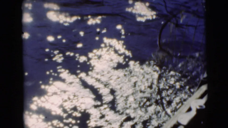 1953 8mm fishing-scene frame from Baraboo with bright water reflections near a pale boat or dock edge.