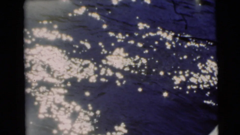 1953 Baraboo home-movie frame showing rippling blue water, bright highlights, and a pale boat or dock edge at lower right.
