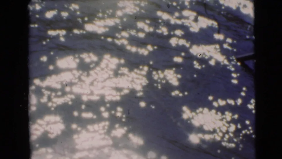 1953 8mm frame from Baraboo, Wisconsin showing bright sunlight sparkling on rippled river water.